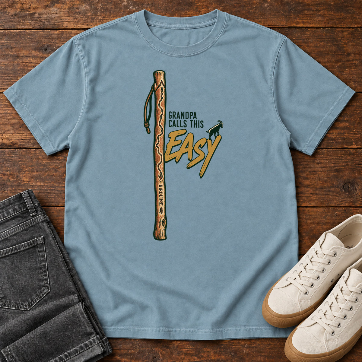 Ice Blue Grandpa Calls This Easy T-Shirt with a wooden hiking stick beside green-and-gold lettering and a small goat silhouette; front flat lay on wood.