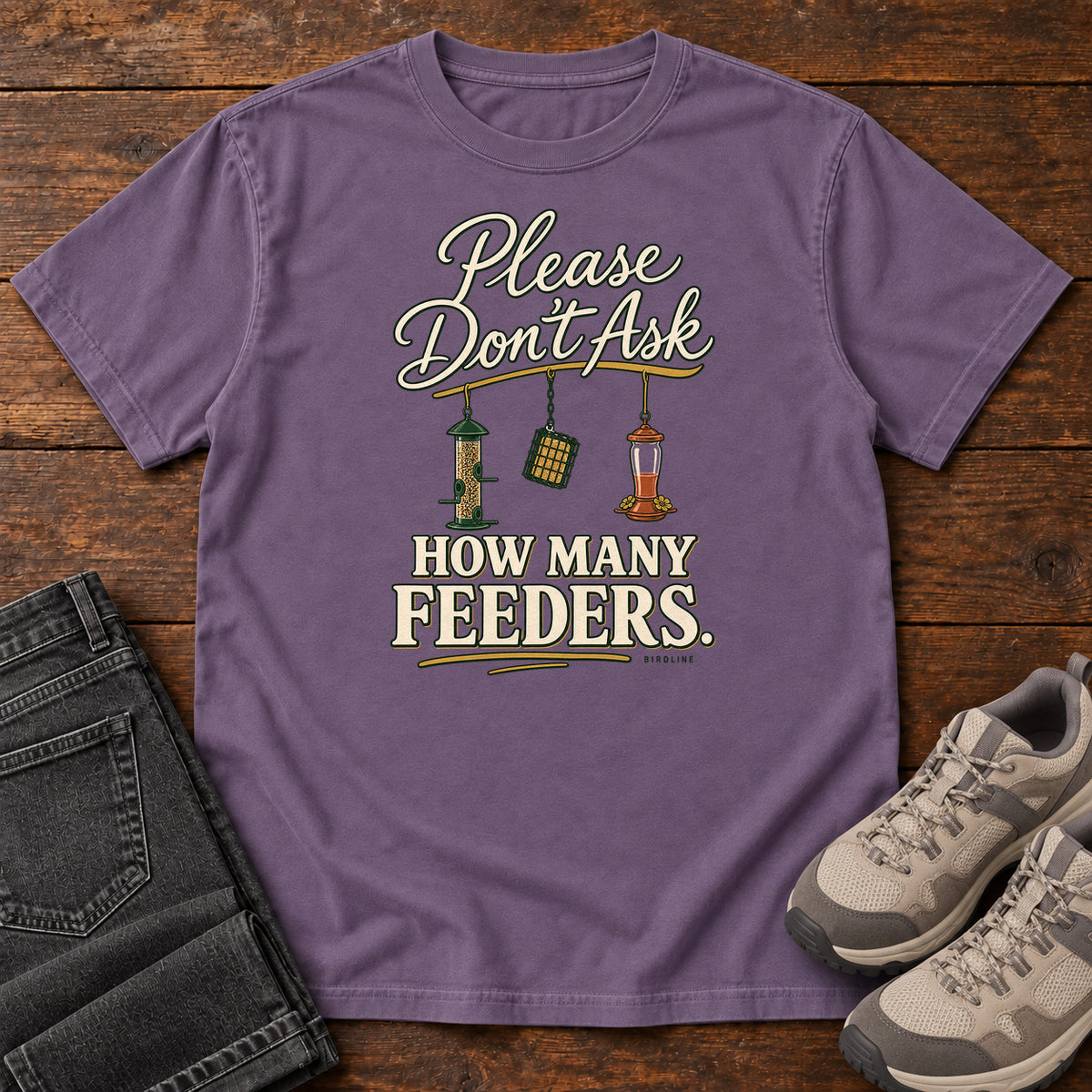 Grape Please Don't Ask How Many Feeders T-Shirt with cream lettering and three hanging bird feeders, front flat lay on wood.