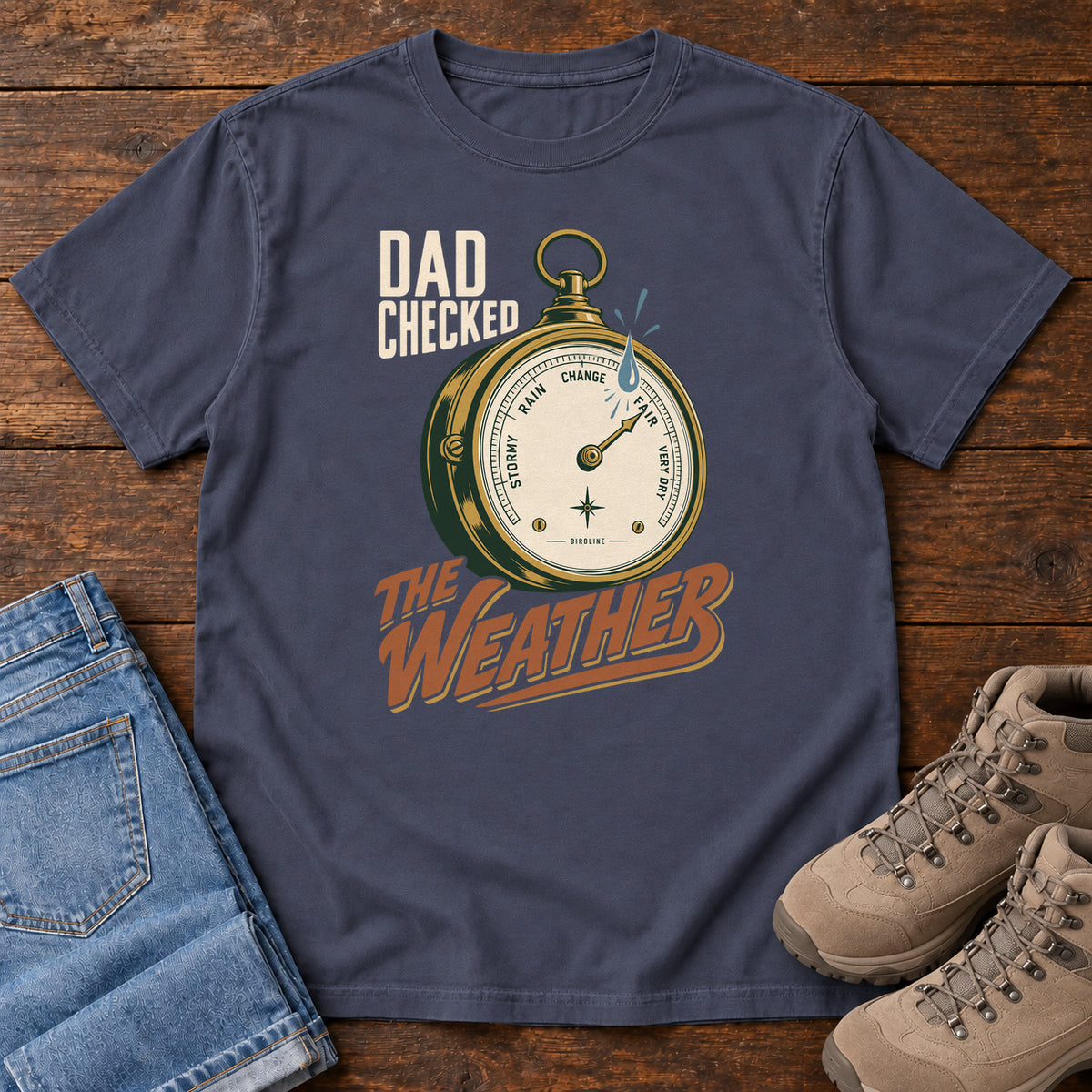 Navy Dad Checked the Weather T-shirt with a weather dial graphic and lettering, laid flat on a wooden surface.