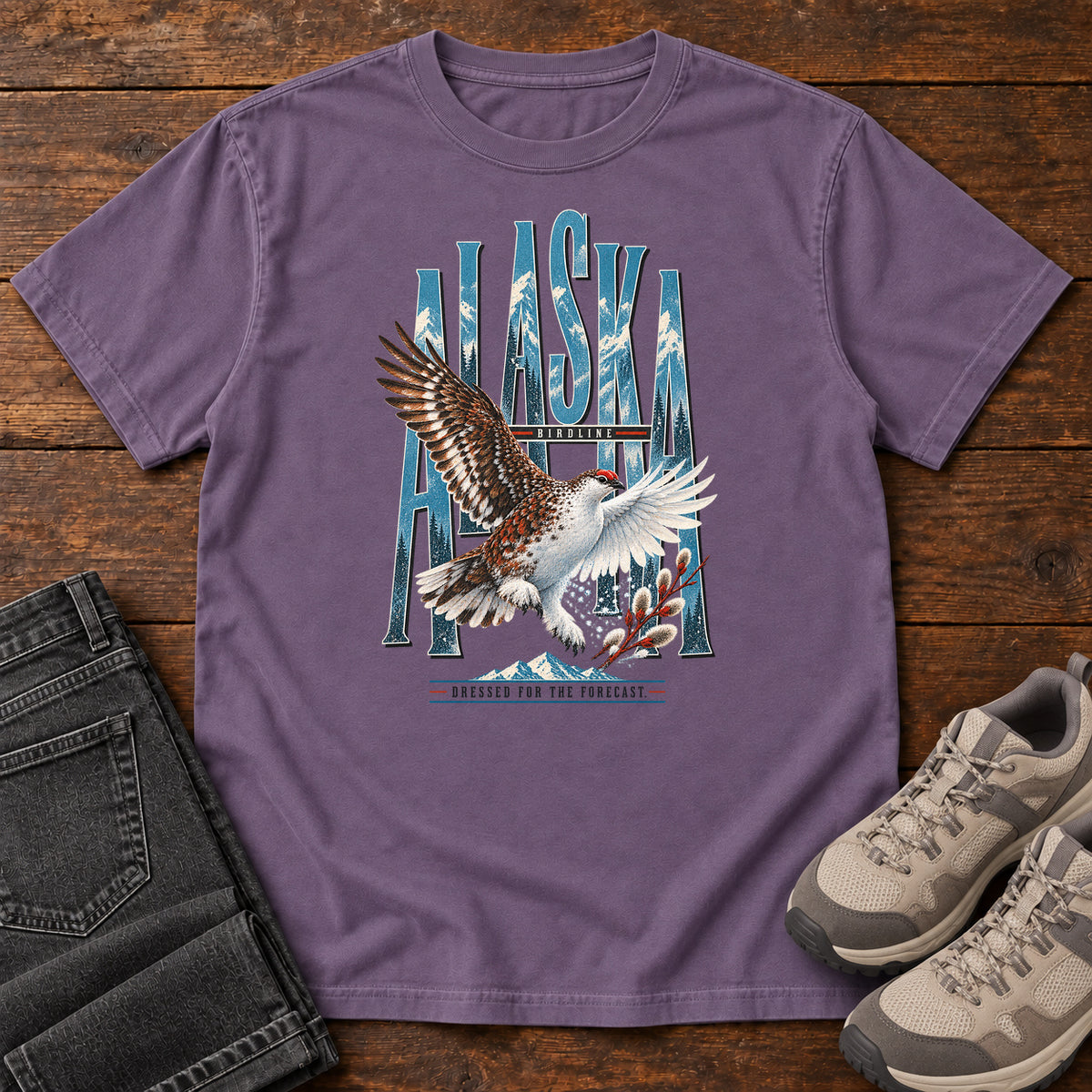 Grape Alaska Dressed for the Forecast Eagle T-Shirt with a white-and-brown bird with raised wings over Alaska lettering and snowy mountains; front flat lay on wood.