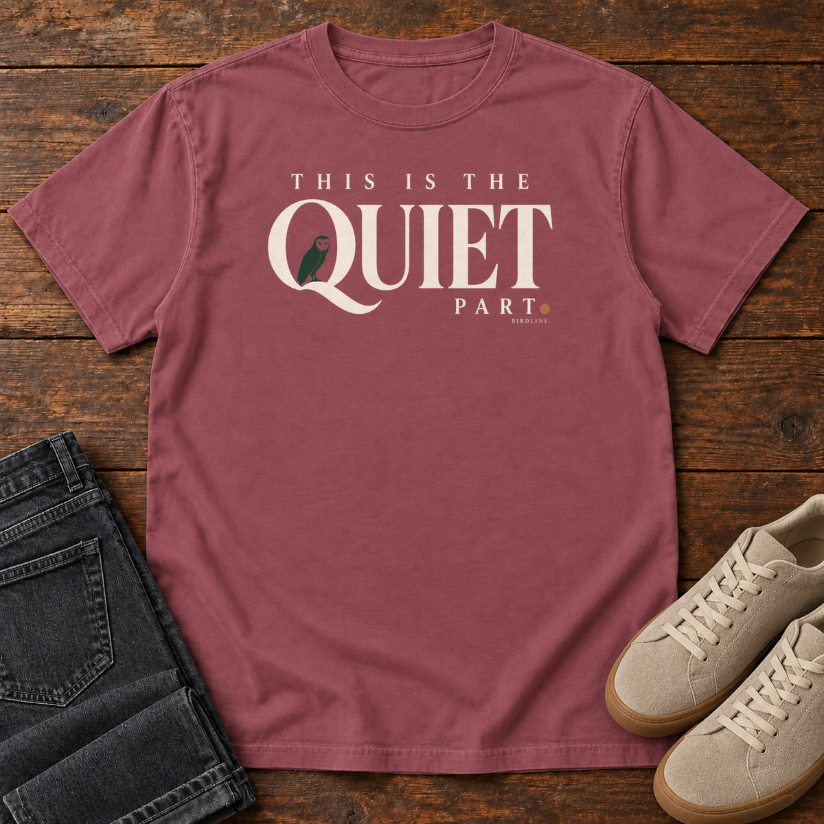 Brick This Is the Quiet Part T-Shirt with cream This Is the Quiet Part lettering with a small green bird inside the Q, front flat lay on wood.