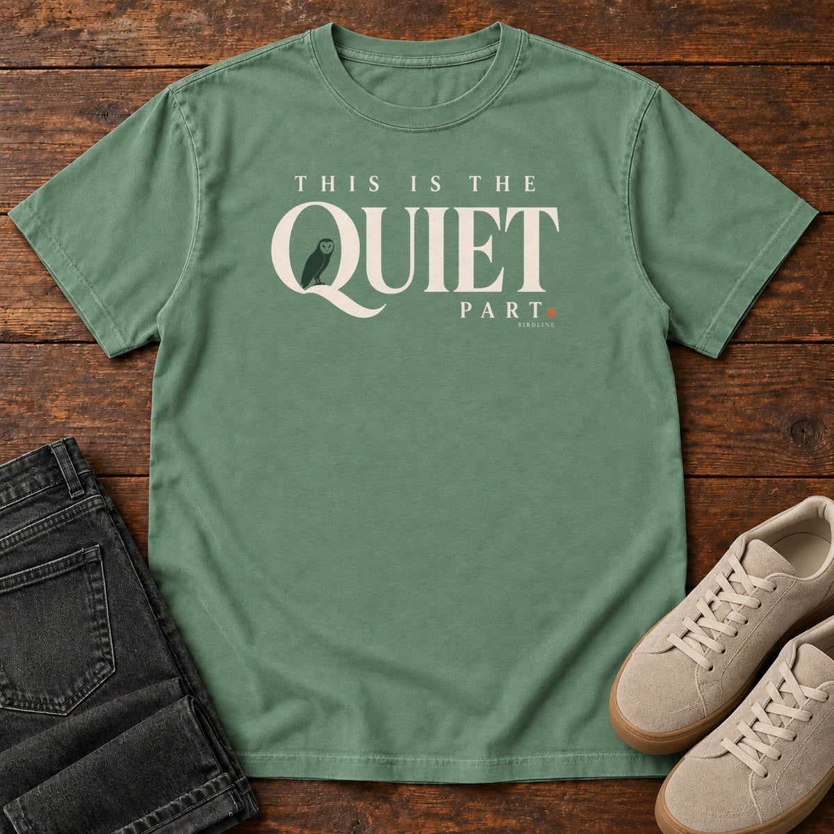 Light Green This Is the Quiet Part T-Shirt with cream This Is the Quiet Part lettering with a small green bird inside the Q, front flat lay on wood.