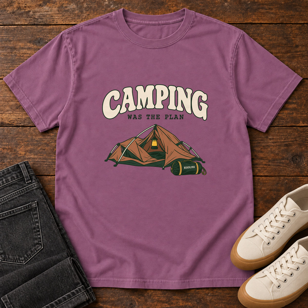 Berry Camping Was the Plan T-Shirt with an orange tent with a hanging lantern and green gear bag; front flat lay on wood.