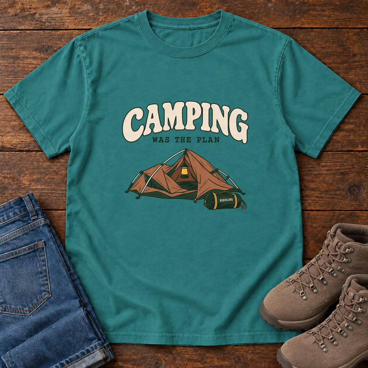 Emerald Camping Was the Plan T-Shirt with an orange tent with a hanging lantern and green gear bag; front flat lay on wood.
