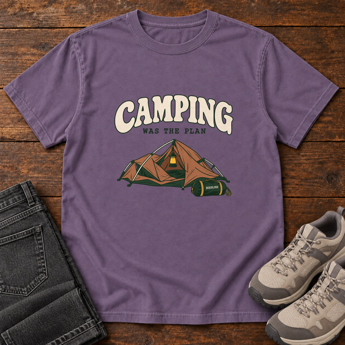Grape Camping Was the Plan T-Shirt with an orange tent with a hanging lantern and green gear bag; front flat lay on wood.