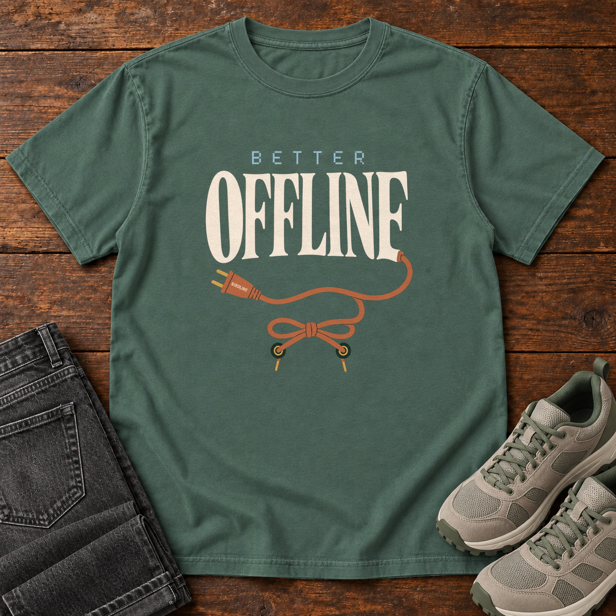 Blue Spruce Better Offline T-Shirt with cream Better Offline lettering and an orange unplugged cord; front flat lay on wood.