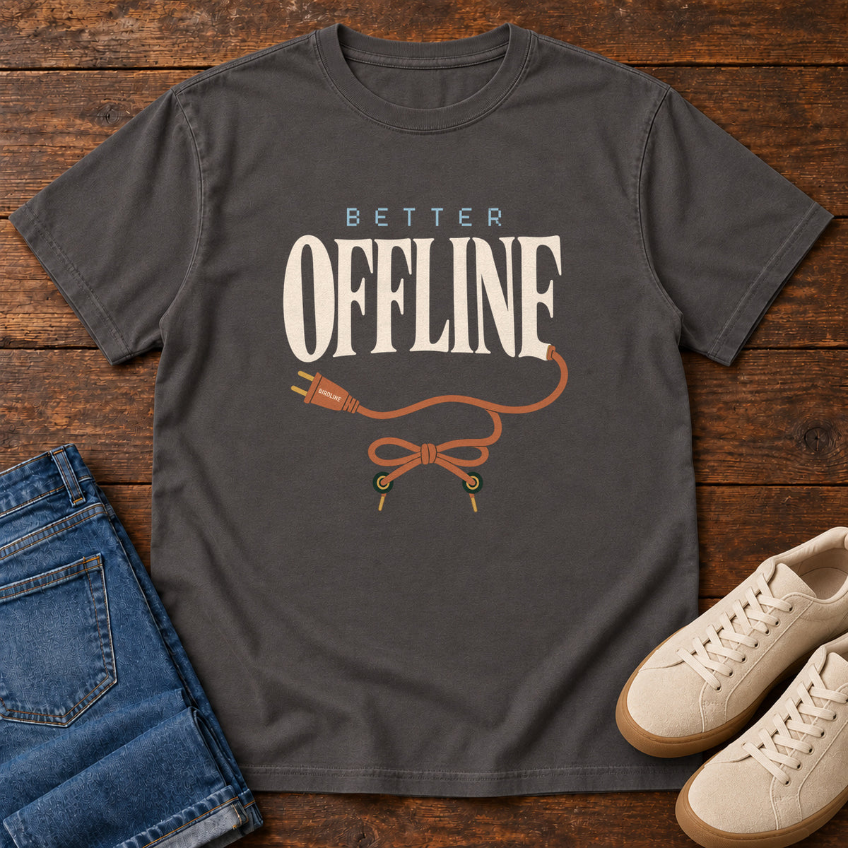 Graphite Better Offline T-Shirt with cream Better Offline lettering and an orange unplugged cord; front flat lay on wood.