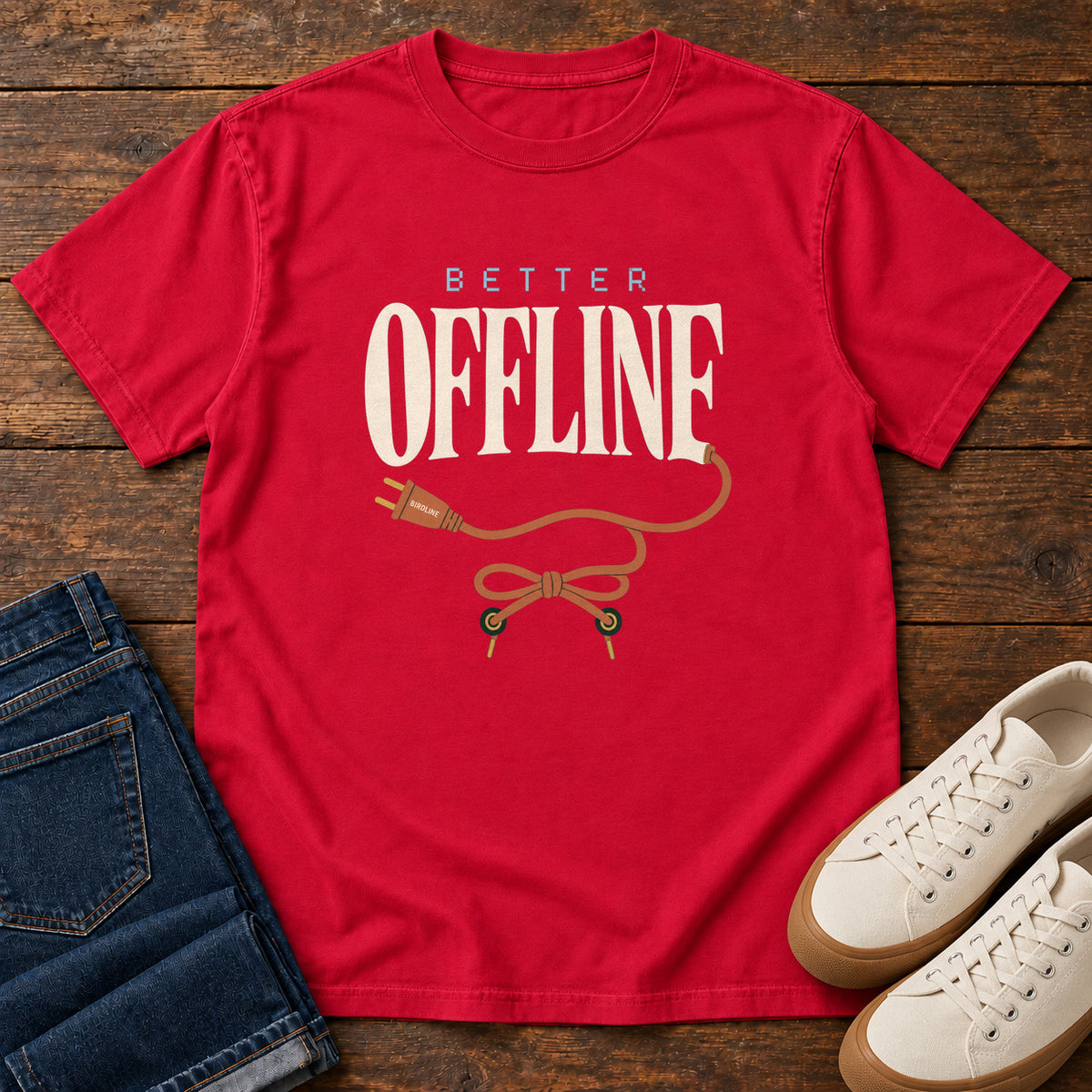 Red Better Offline T-Shirt with cream Better Offline lettering and an orange unplugged cord; front flat lay on wood.
