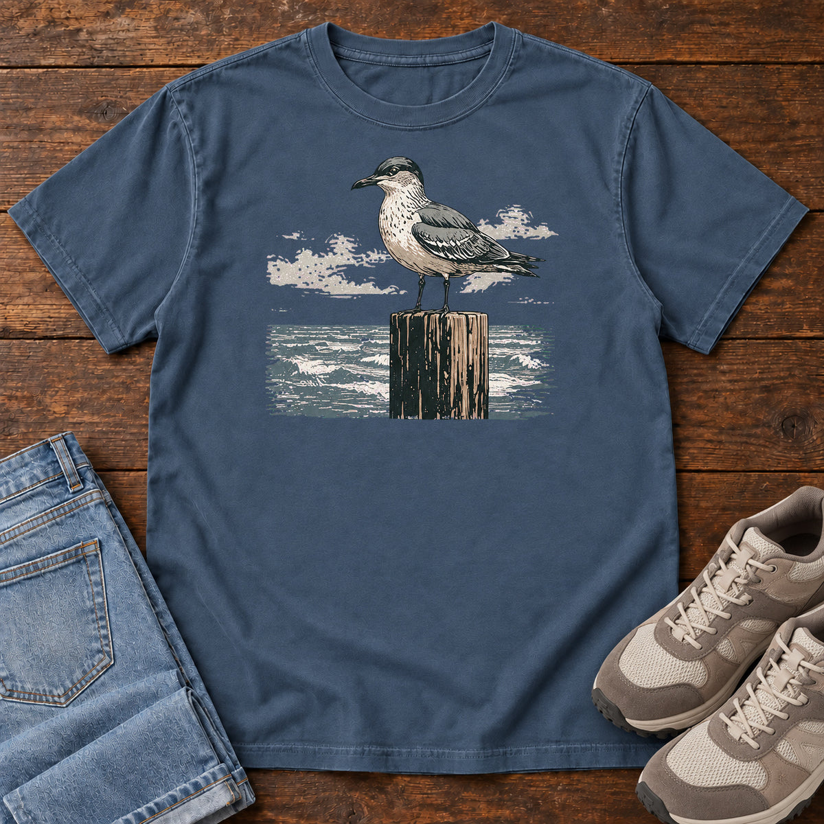 Midnight Gull On A Piling T-shirt with a gull standing on a wooden piling above the water, laid flat on a wooden surface.