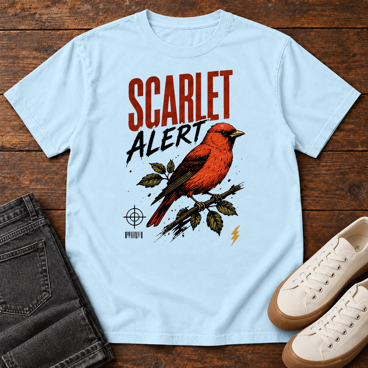 Chambray Scarlet Alert T-shirt with a red bird on a branch and Scarlet Alert lettering, laid flat on a wooden surface.