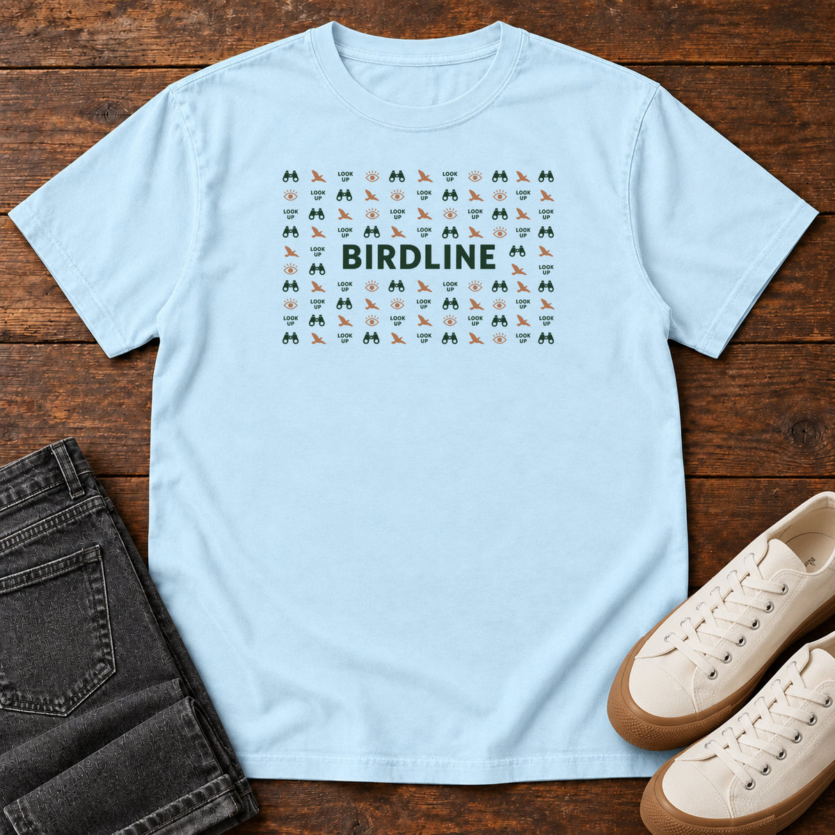 Chambray Look Up Micro Pattern T-shirt with small binocular, bird and eye icons around green Birdline lettering; front flat lay on wood.
