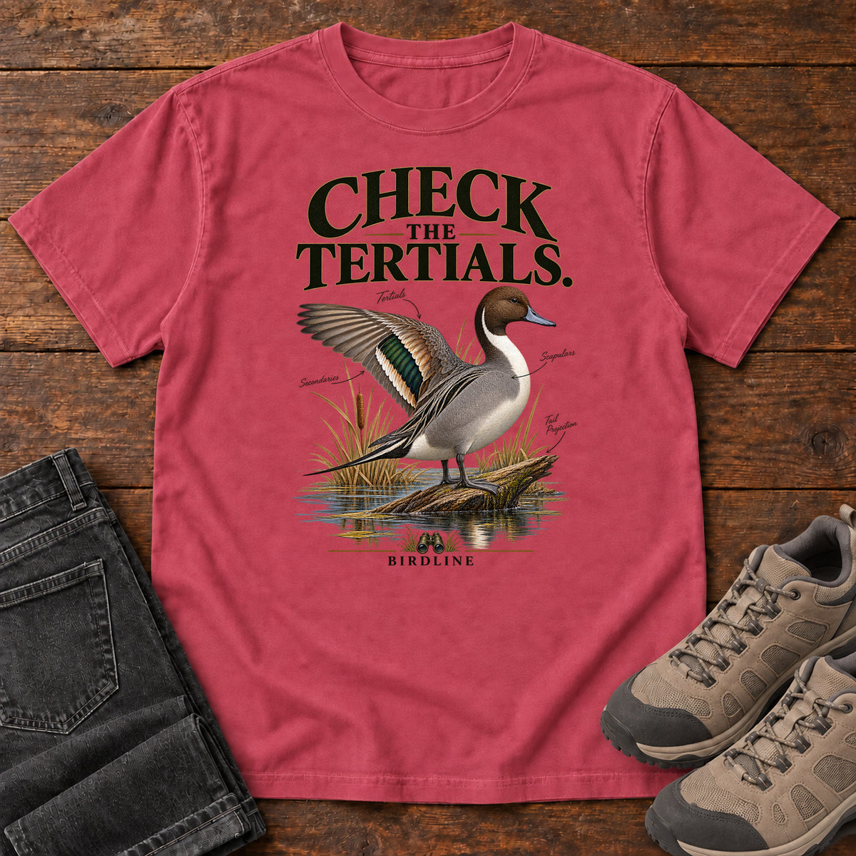 Paprika Check the Tertials Duck T-Shirt with a duck raising one wing beside reeds and water; front flat lay on wood.