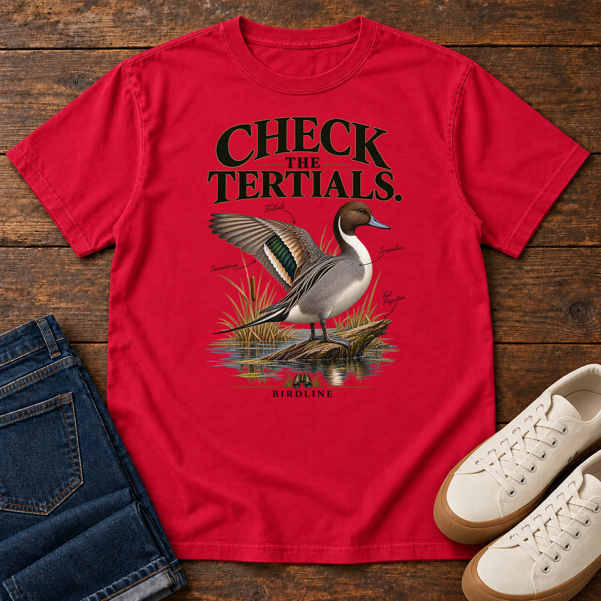 Red Check the Tertials Duck T-Shirt with a duck raising one wing beside reeds and water; front flat lay on wood.
