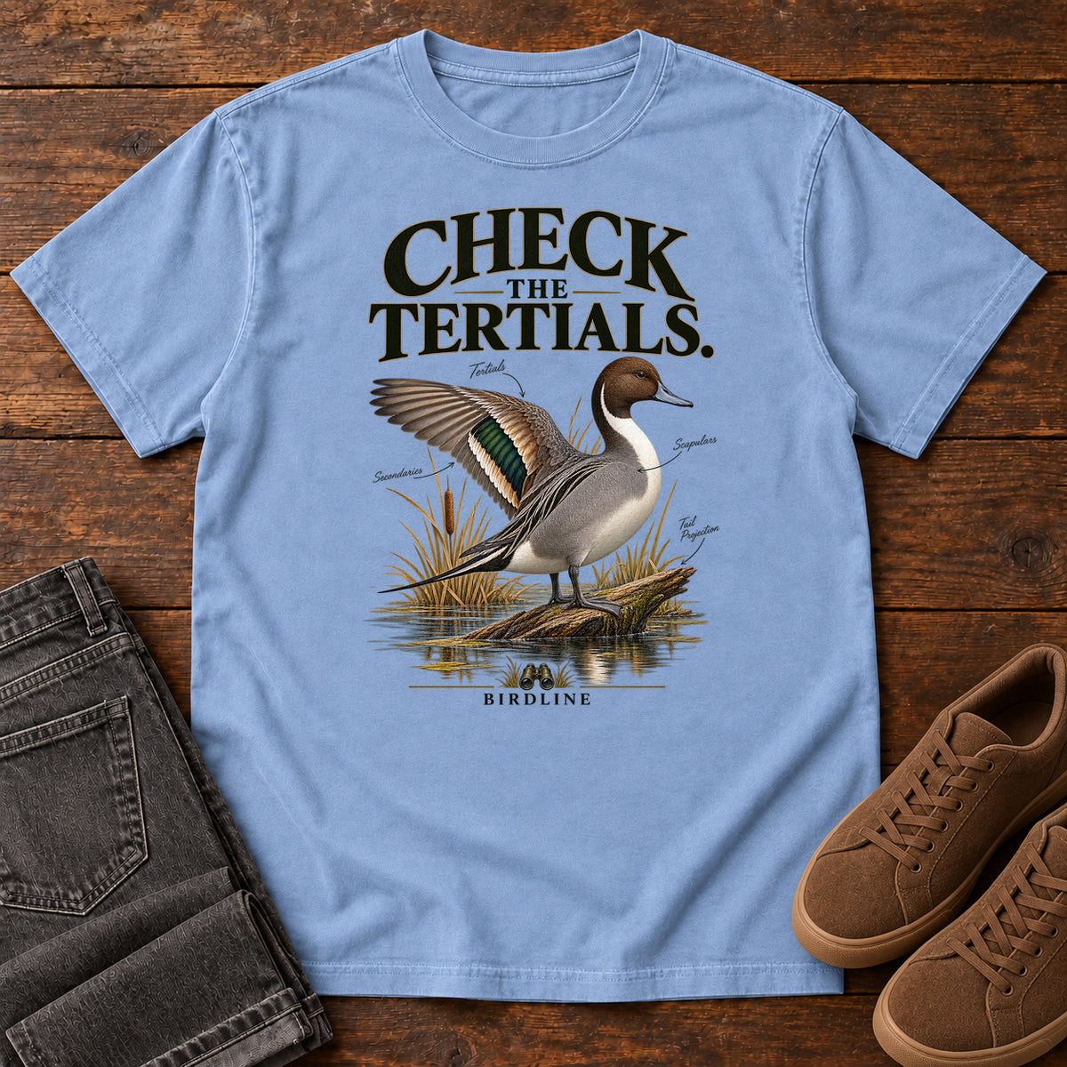 Washed Denim Check the Tertials Duck T-Shirt with a duck raising one wing beside reeds and water; front flat lay on wood.