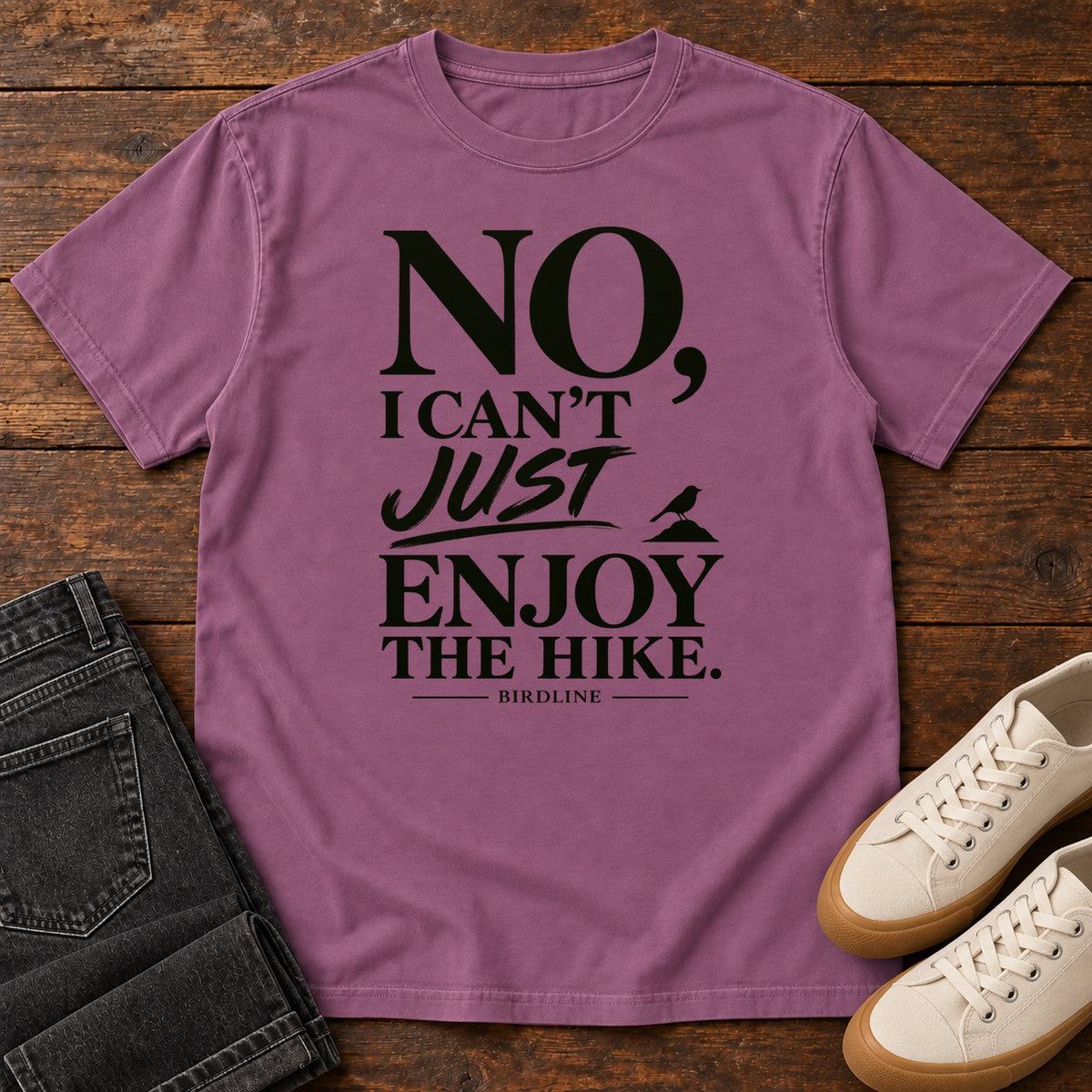 Berry No I Can't Just Enjoy the Hike T-Shirt with bold black lettering and a small bird silhouette, front flat lay on wood.