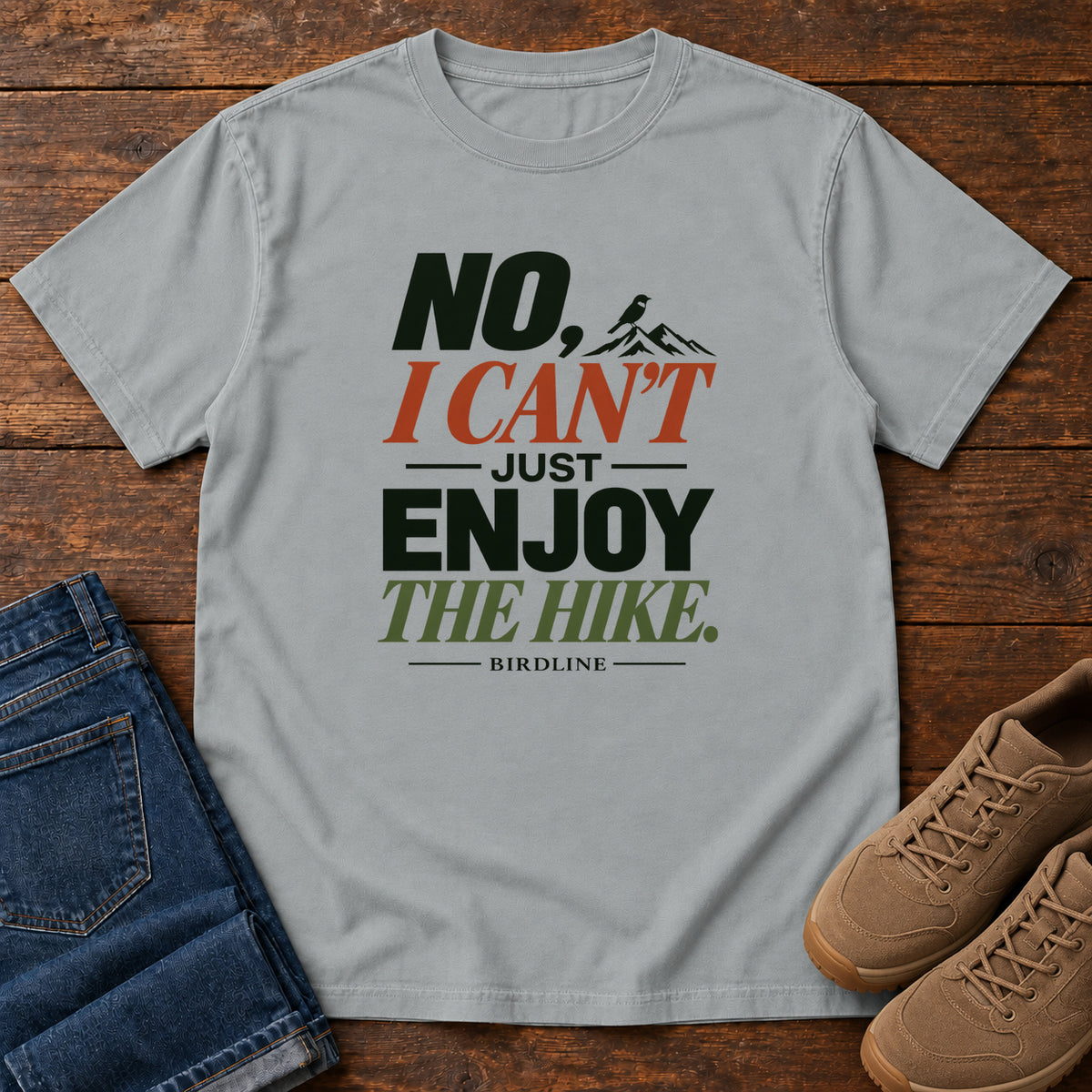 No I Can't Just Enjoy the Hike T-Shirt – Color Block in Granite, front laid flat on wood, featuring stacked green and rust slogan lettering and a small mountain graphic.