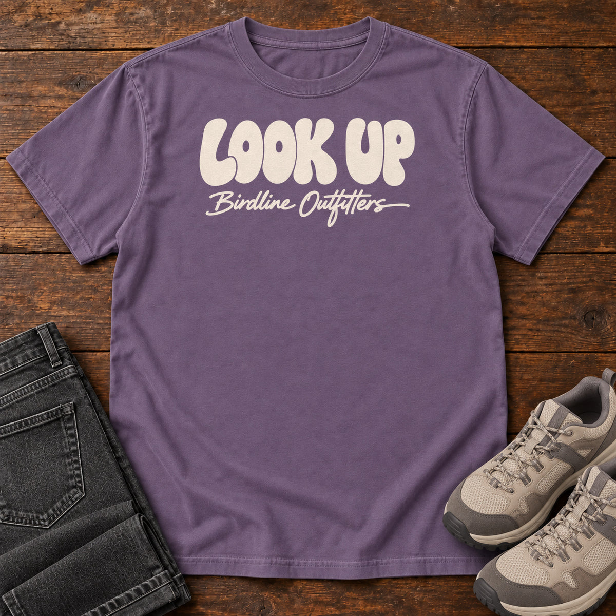 Look Up T-shirt in Grape, front laid flat on wood, featuring large rounded cream LOOK UP lettering above Birdline Outfitters script.