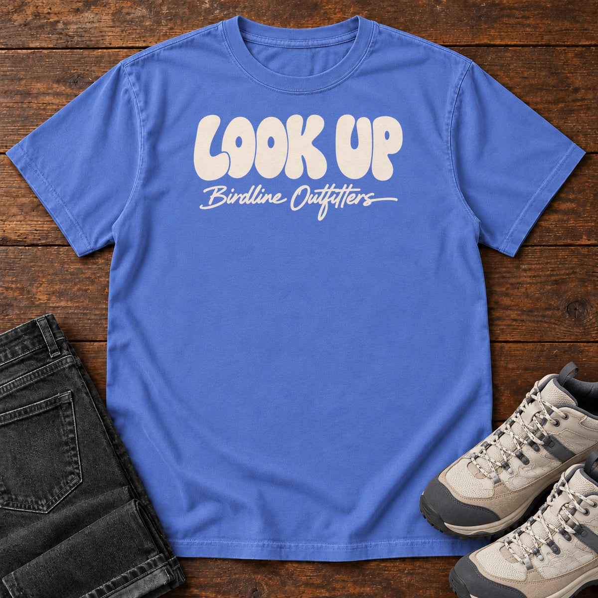 Look Up T-shirt in Mystic Blue, front laid flat on wood, featuring large rounded cream LOOK UP lettering above Birdline Outfitters script.