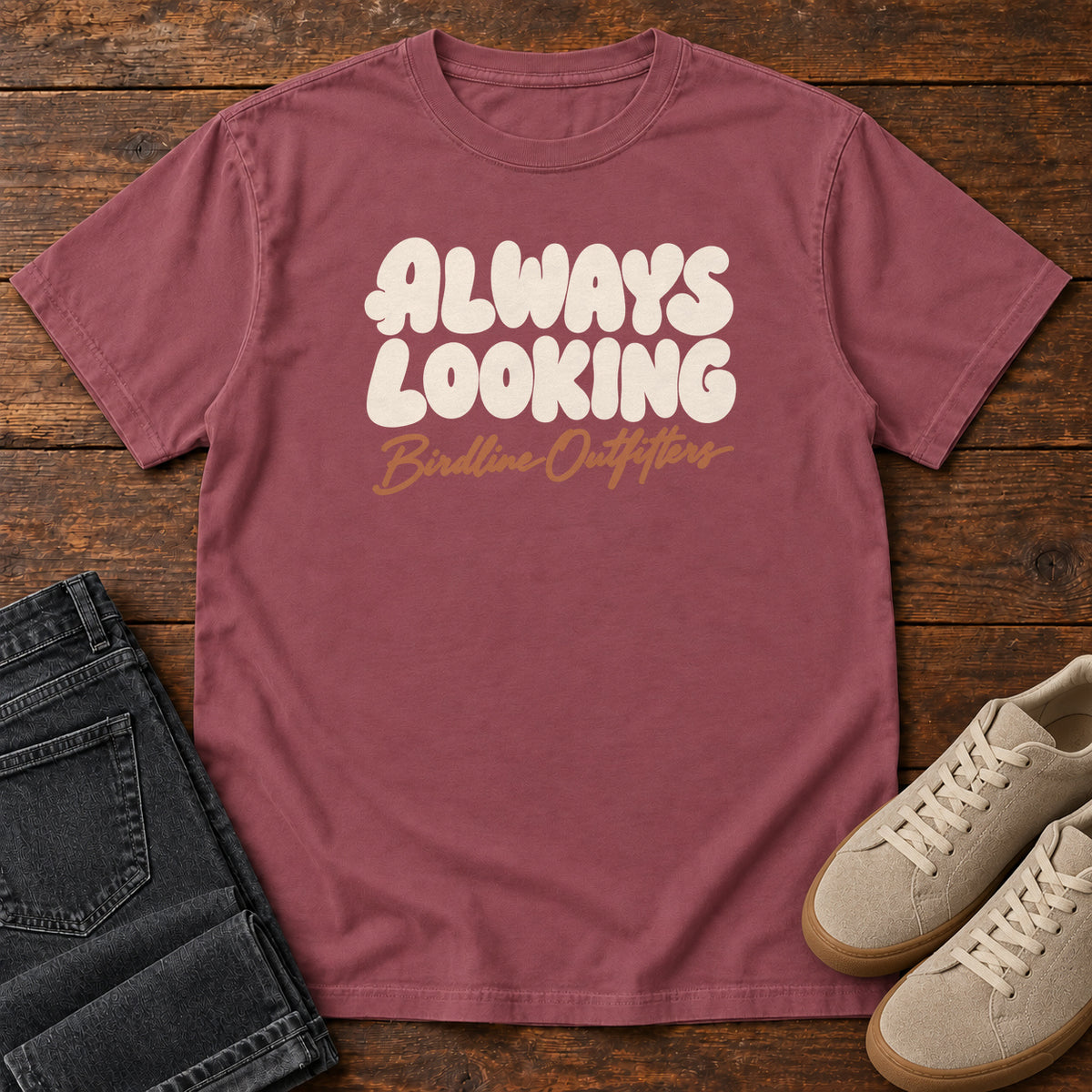 Brick Always Looking T-shirt with cream bubble lettering above an orange Birdline Outfitters script; front flat lay on wood.
