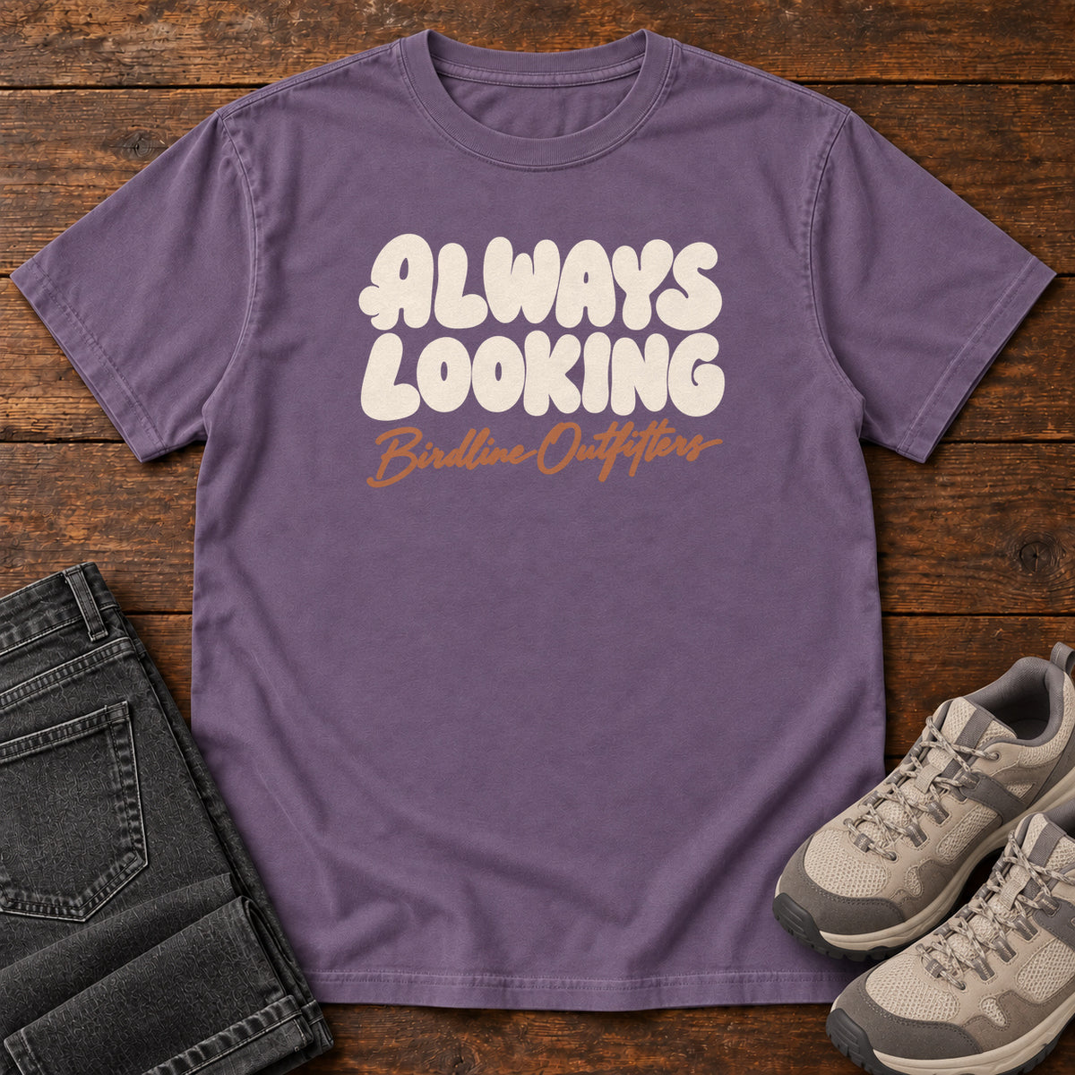 Grape Always Looking T-shirt with cream bubble lettering above an orange Birdline Outfitters script; front flat lay on wood.