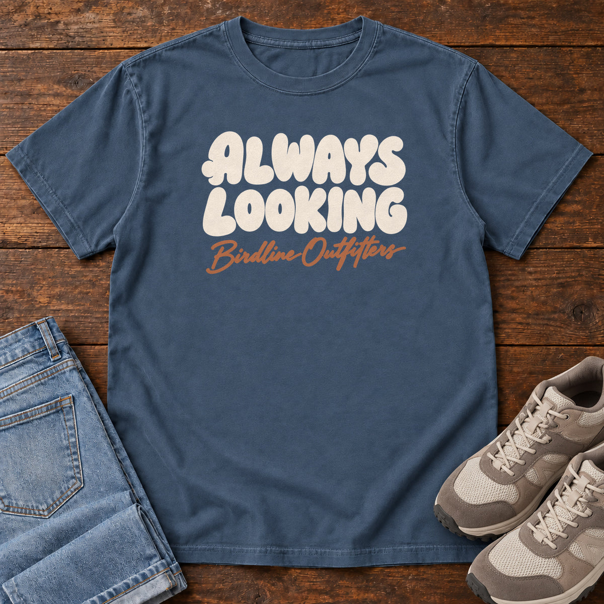 Midnight Always Looking T-shirt with cream bubble lettering above an orange Birdline Outfitters script; front flat lay on wood.