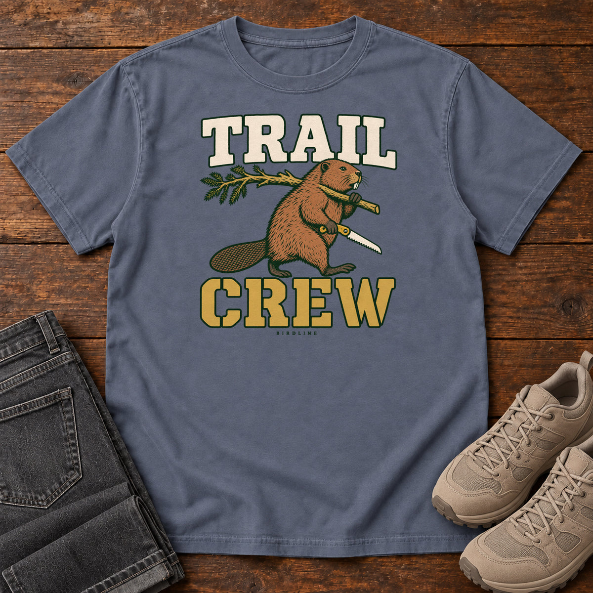 Denim Trail Crew Foreman T-Shirt with a beaver carrying a leafy branch and saw beneath Trail Crew lettering; front flat lay on wood.