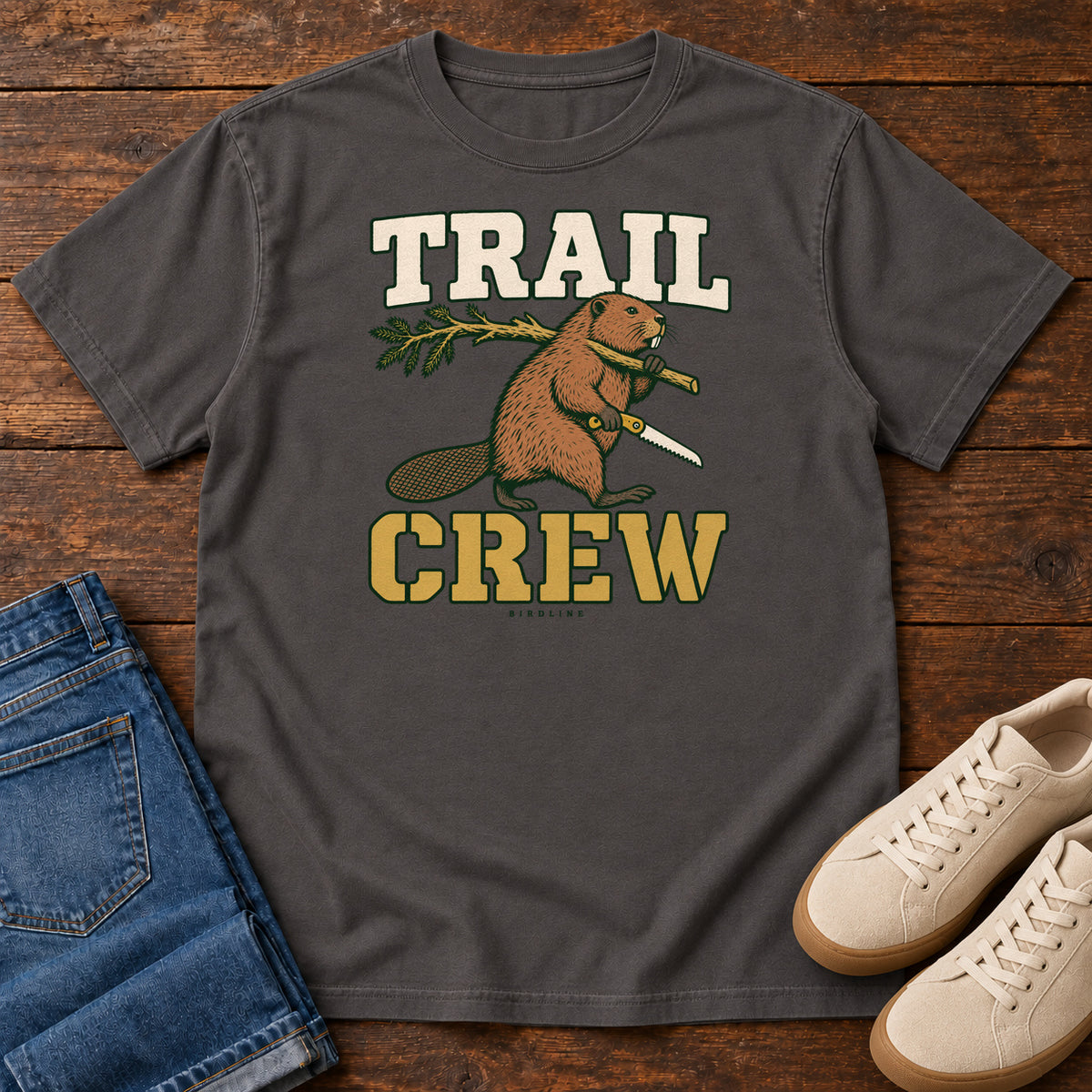 Graphite Trail Crew Foreman T-Shirt with a beaver carrying a leafy branch and saw beneath Trail Crew lettering; front flat lay on wood.