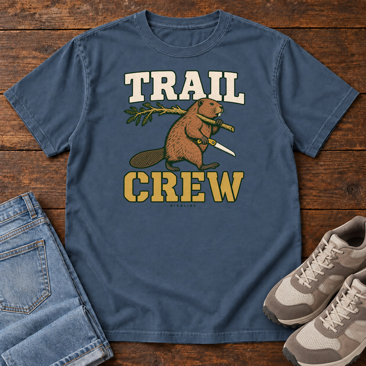 Midnight Trail Crew Foreman T-Shirt with a beaver carrying a leafy branch and saw beneath Trail Crew lettering; front flat lay on wood.