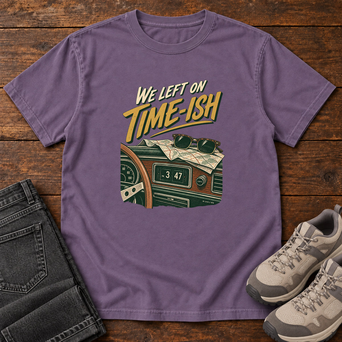 Grape We Left on Time-Ish T-Shirt with a retro dashboard, folded map and sunglasses; front flat lay on wood.