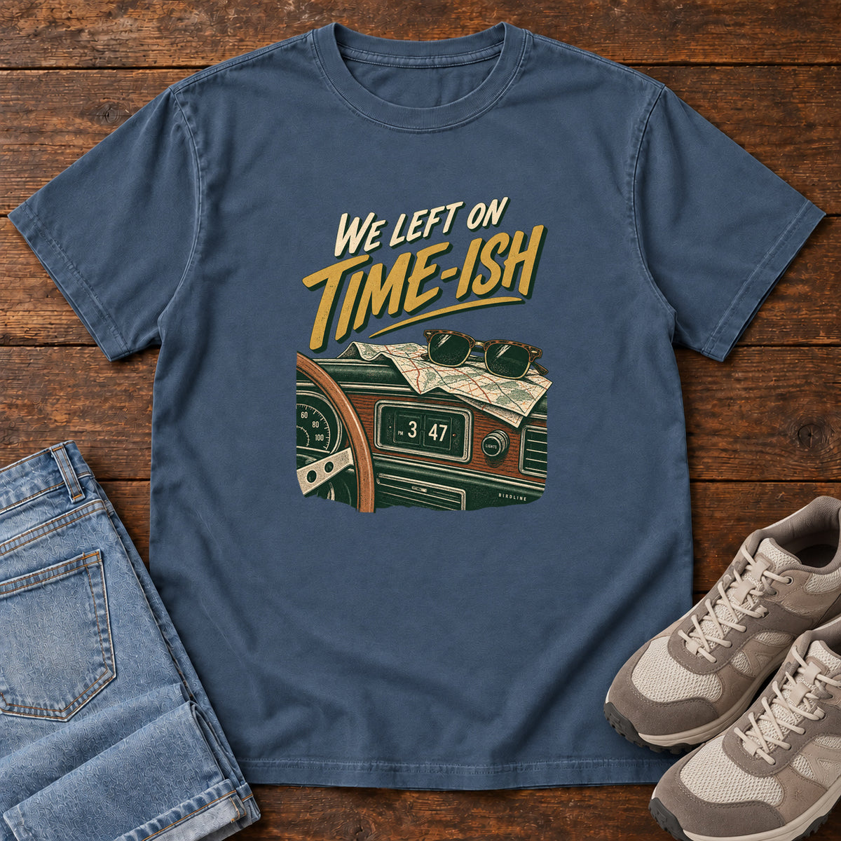 Midnight We Left on Time-Ish T-Shirt with a retro dashboard, folded map and sunglasses; front flat lay on wood.