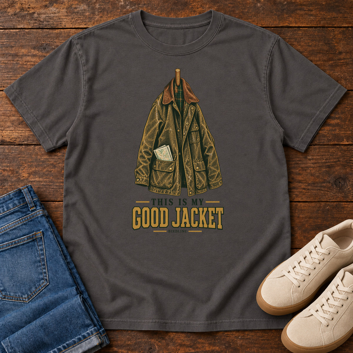 Graphite This Is My Good Jacket T-Shirt with a hanging outdoor jacket and This Is My Good Jacket lettering; front flat lay on wood.