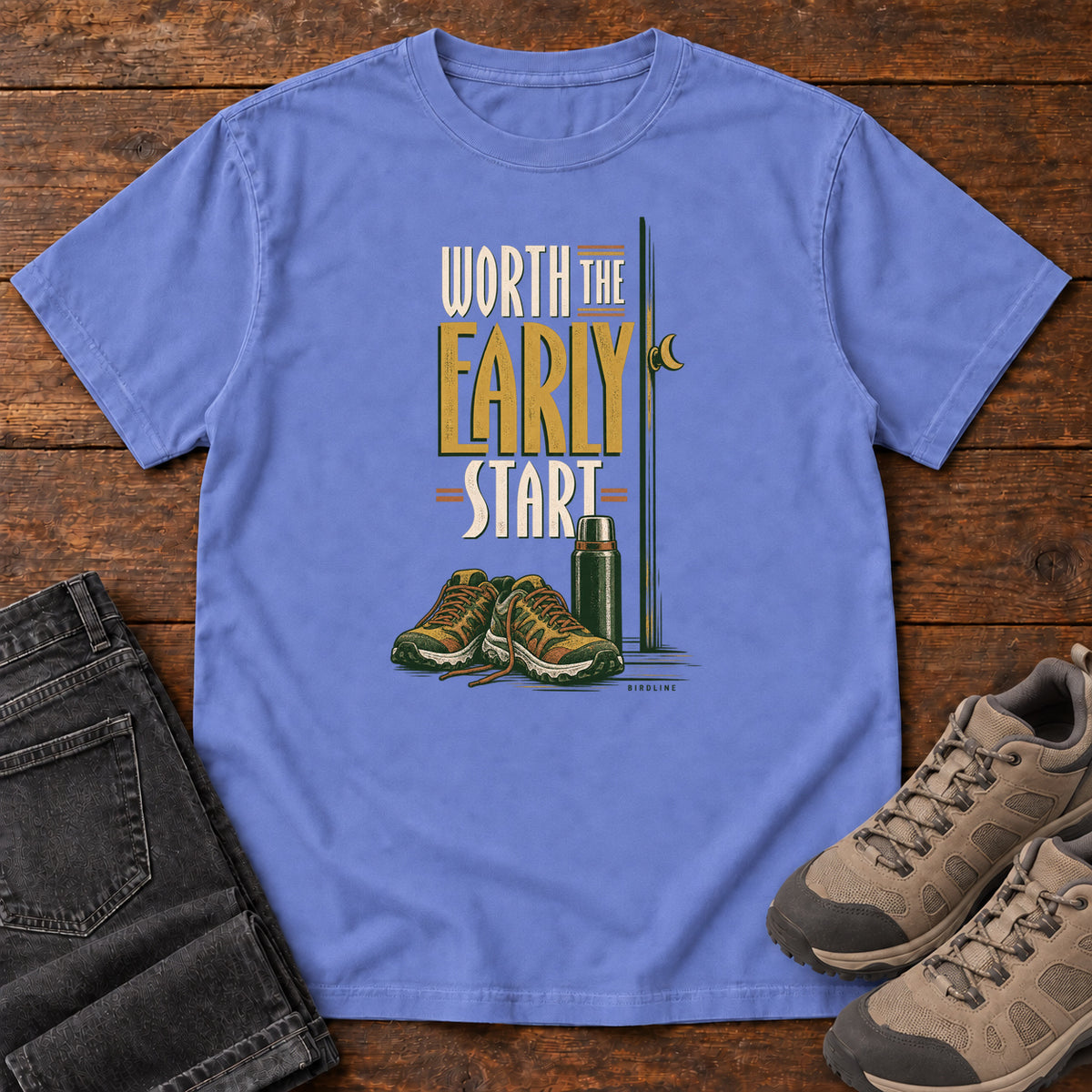 Flo Blue Worth the Early Start T-Shirt with hiking shoes, a thermos, a walking pole and a crescent moon; front flat lay on wood.
