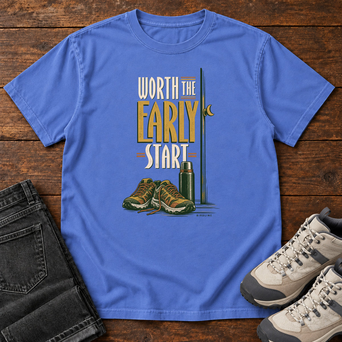 Mystic Blue Worth the Early Start T-Shirt with hiking shoes, a thermos, a walking pole and a crescent moon; front flat lay on wood.