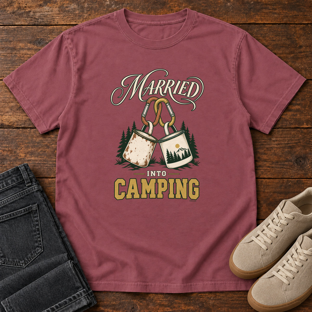 Brick Married into Camping T-Shirt with two camp mugs hanging from carabiners between cream and gold lettering, front flat lay on wood.