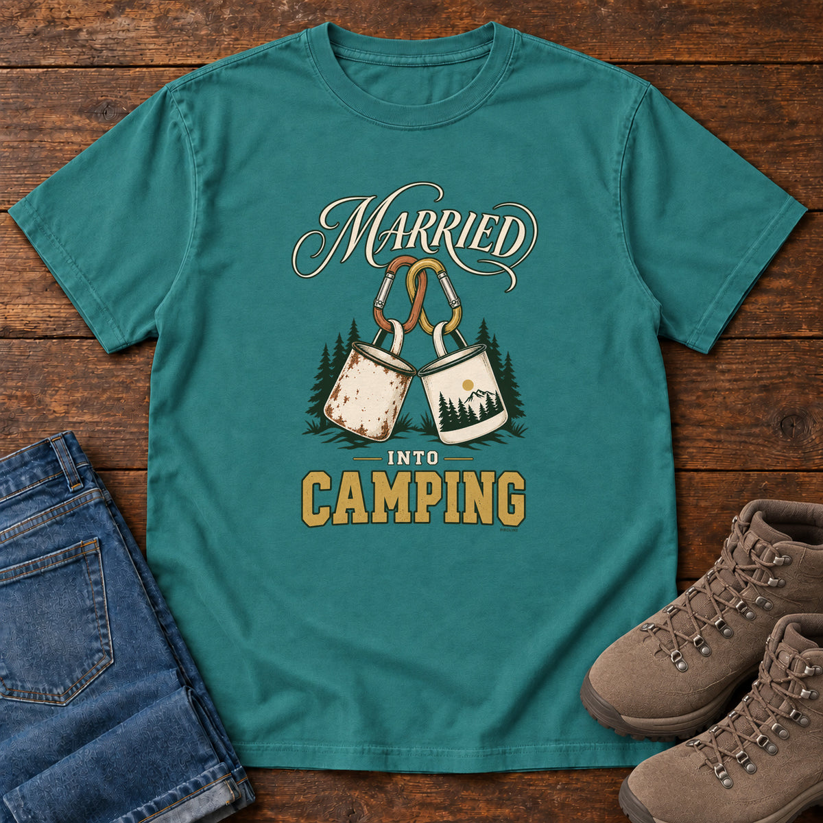 Emerald Married into Camping T-Shirt with two camp mugs hanging from carabiners between cream and gold lettering, front flat lay on wood.