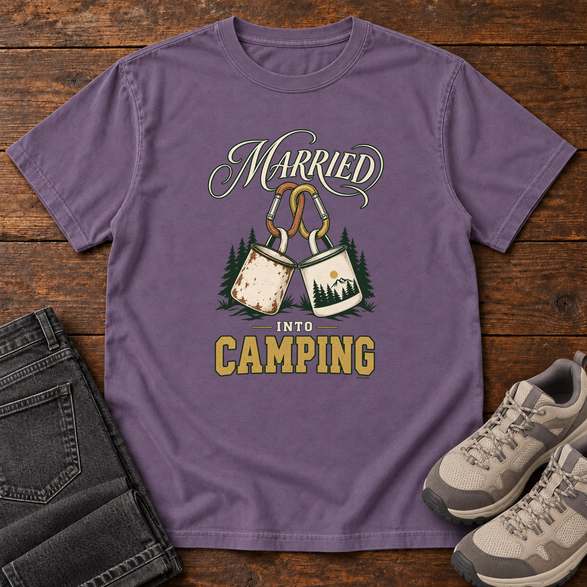Grape Married into Camping T-Shirt with two camp mugs hanging from carabiners between cream and gold lettering, front flat lay on wood.