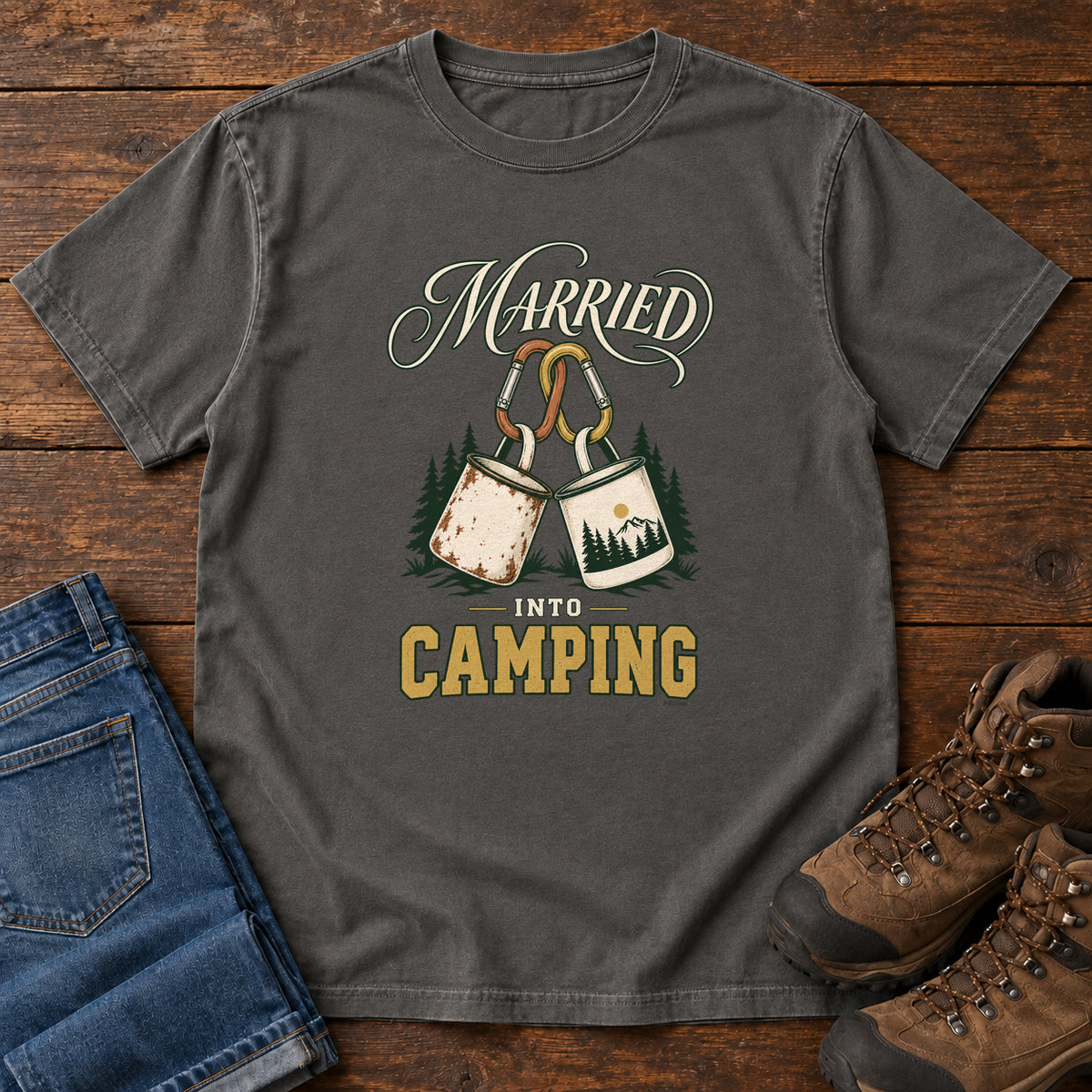 Pepper Married into Camping T-Shirt with two camp mugs hanging from carabiners between cream and gold lettering, front flat lay on wood.