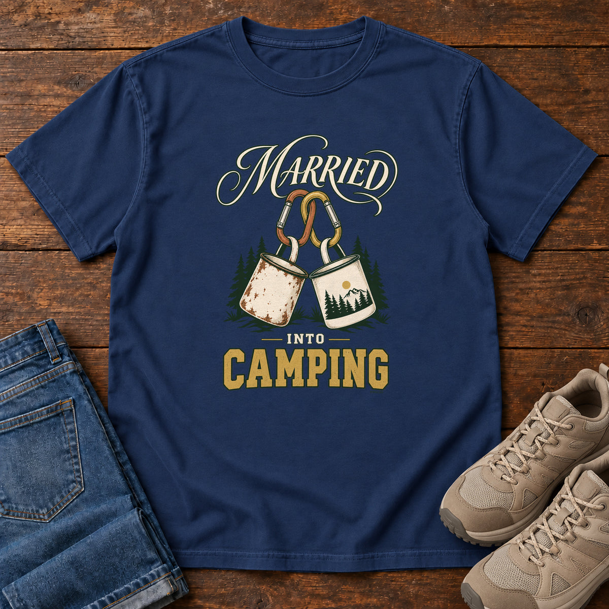 True Navy Married into Camping T-Shirt with two camp mugs hanging from carabiners between cream and gold lettering, front flat lay on wood.
