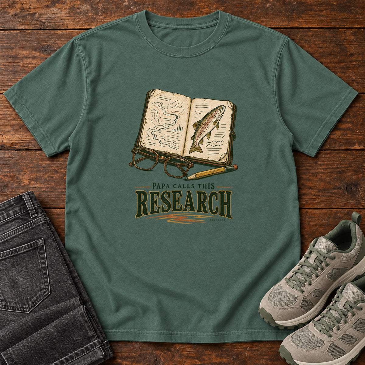 Blue Spruce Papa Calls This Research T-Shirt with an open field notebook showing a map and fish, with glasses and a pencil, front flat lay on wood.