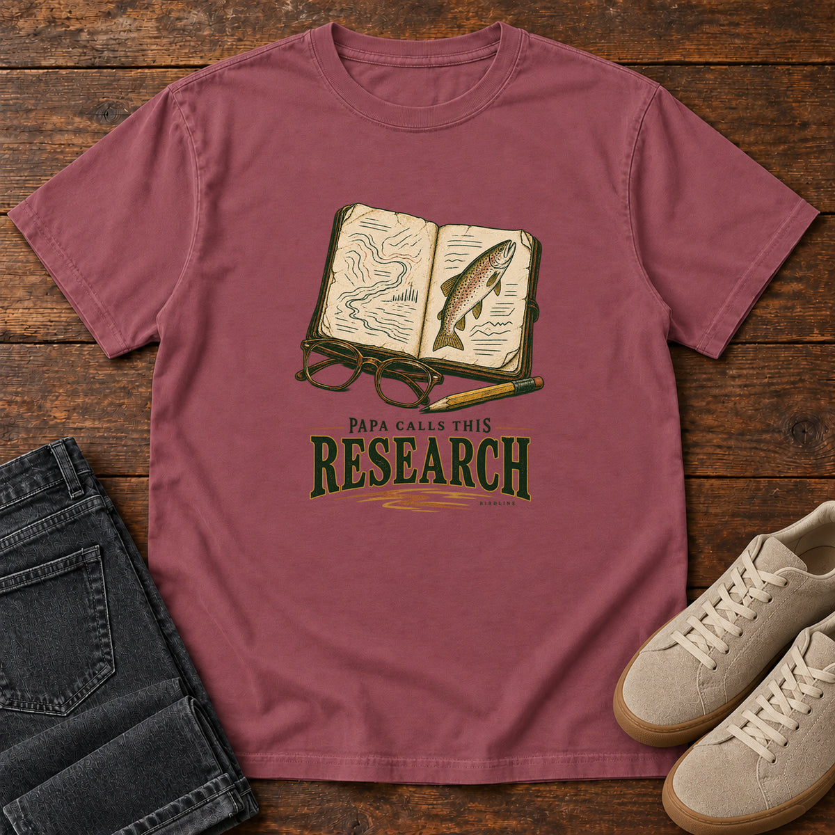 Brick Papa Calls This Research T-Shirt with an open field notebook showing a map and fish, with glasses and a pencil, front flat lay on wood.