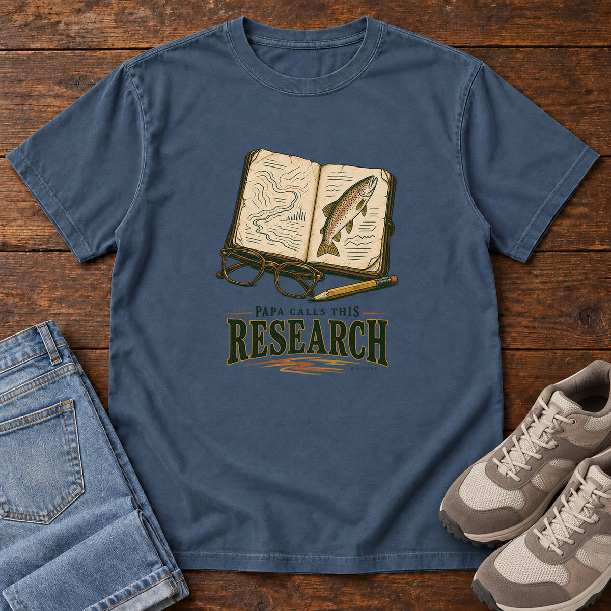 Midnight Papa Calls This Research T-Shirt with an open field notebook showing a map and fish, with glasses and a pencil, front flat lay on wood.