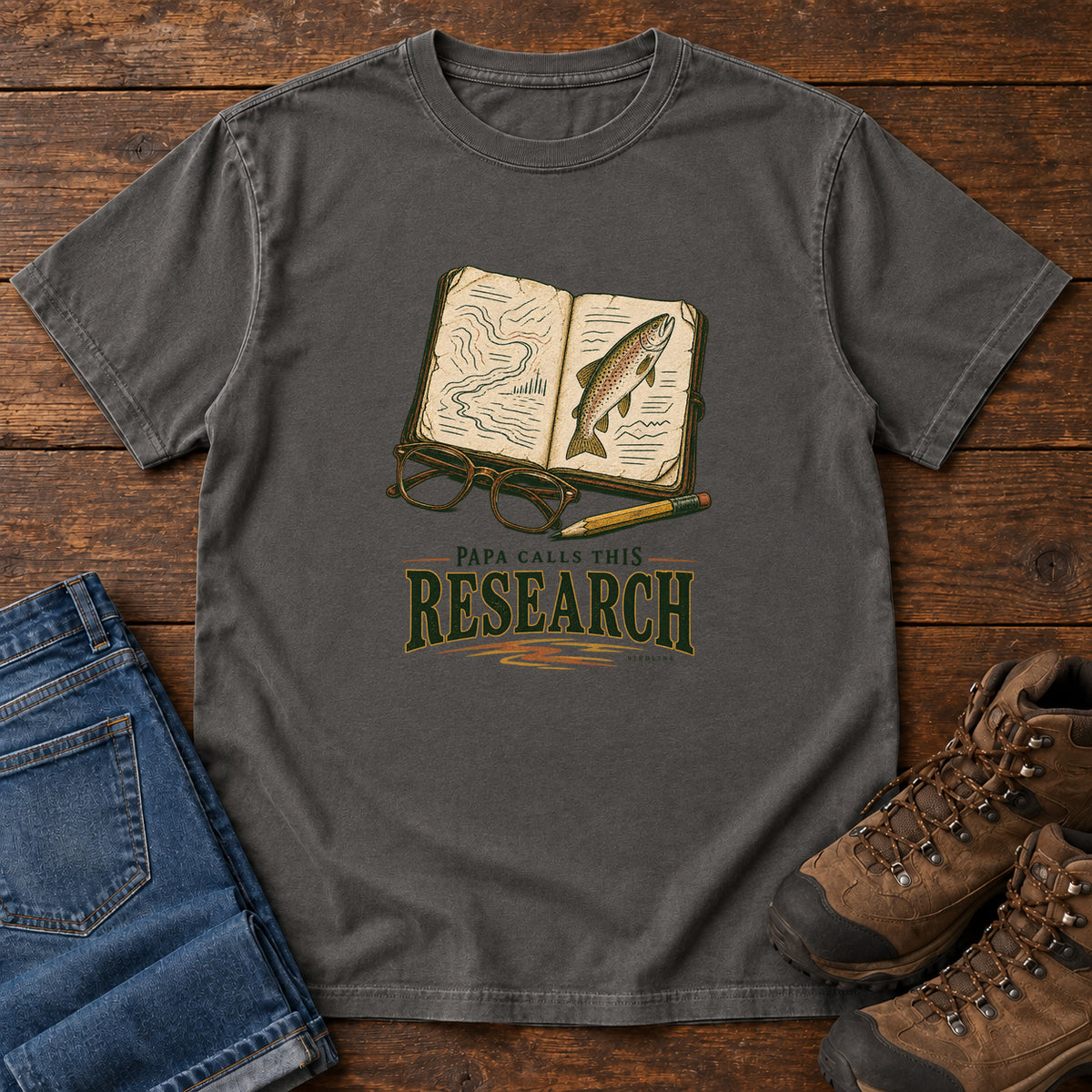 Pepper Papa Calls This Research T-Shirt with an open field notebook showing a map and fish, with glasses and a pencil, front flat lay on wood.