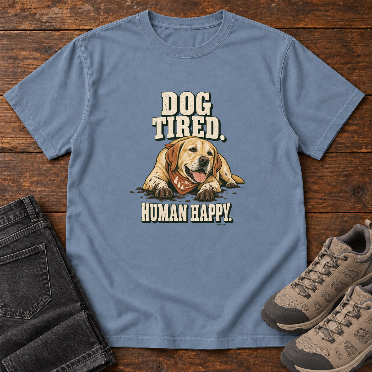 Dog Tired Human Happy T-Shirt in Blue Jean, front laid flat on wood, featuring a resting golden-brown dog wearing an orange bandana between cream slogan lettering.
