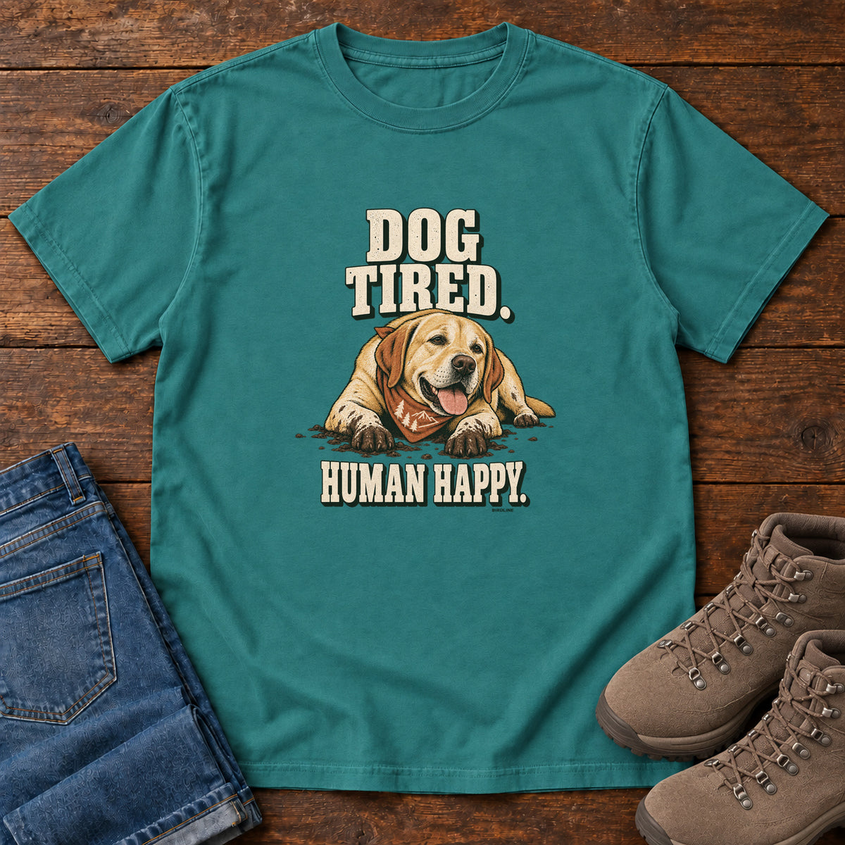 Dog Tired Human Happy T-Shirt in Emerald, front laid flat on wood, featuring a resting golden-brown dog wearing an orange bandana between cream slogan lettering.