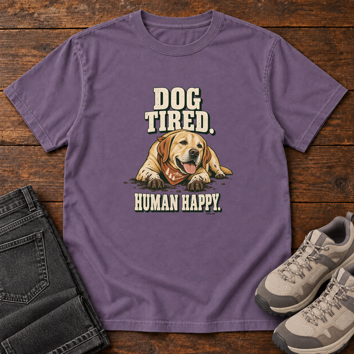 Dog Tired Human Happy T-Shirt in Grape, front laid flat on wood, featuring a resting golden-brown dog wearing an orange bandana between cream slogan lettering.