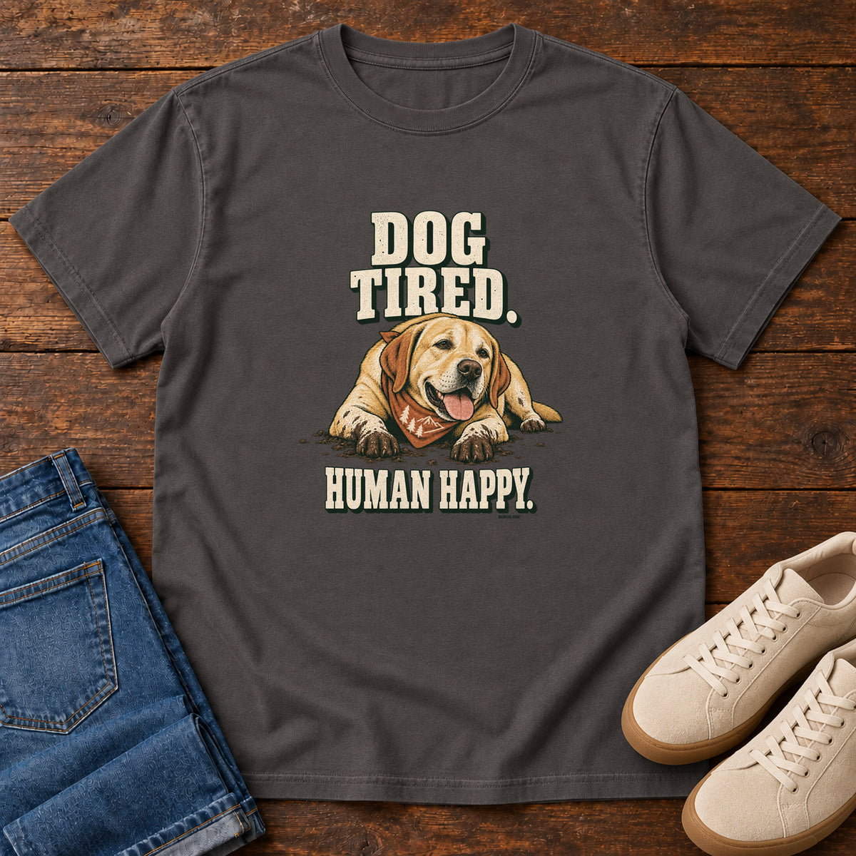 Dog Tired Human Happy T-Shirt in Graphite, front laid flat on wood, featuring a resting golden-brown dog wearing an orange bandana between cream slogan lettering.