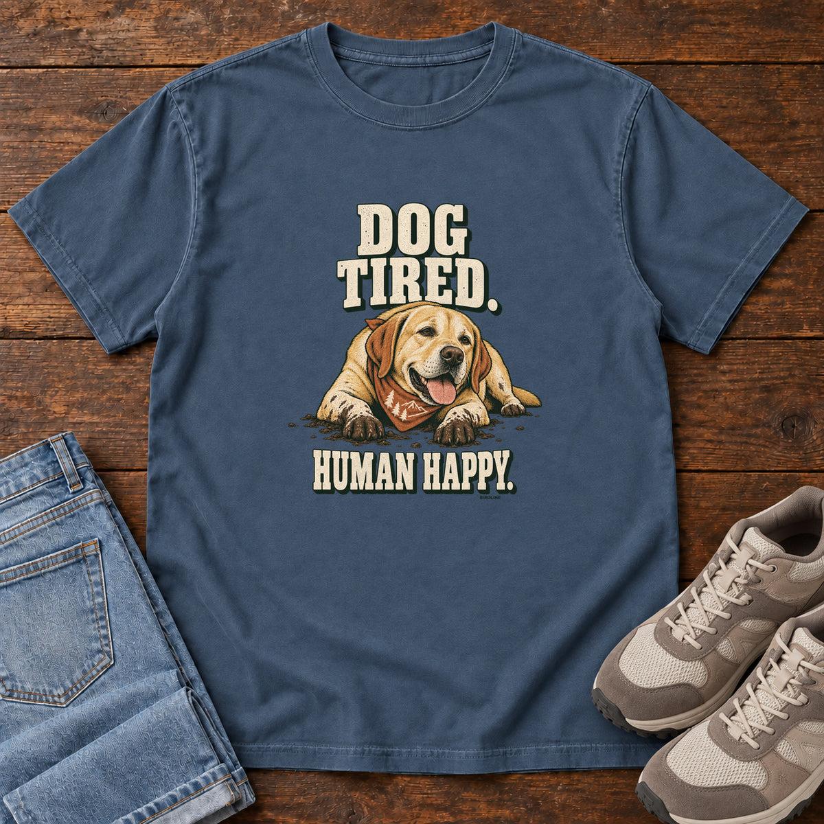 Dog Tired Human Happy T-Shirt in Midnight, front laid flat on wood, featuring a resting golden-brown dog wearing an orange bandana between cream slogan lettering.