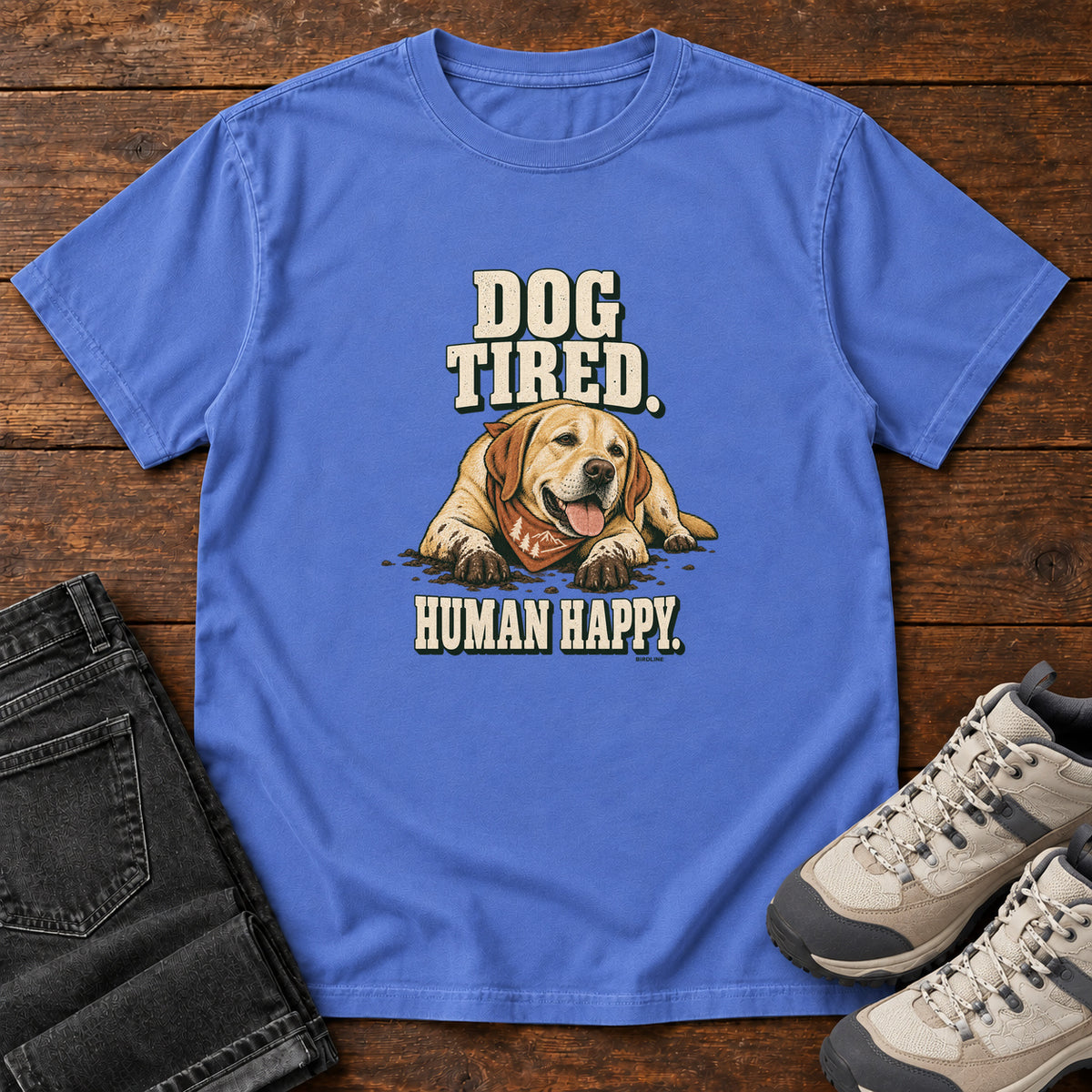 Dog Tired Human Happy T-Shirt in Mystic Blue, front laid flat on wood, featuring a resting golden-brown dog wearing an orange bandana between cream slogan lettering.