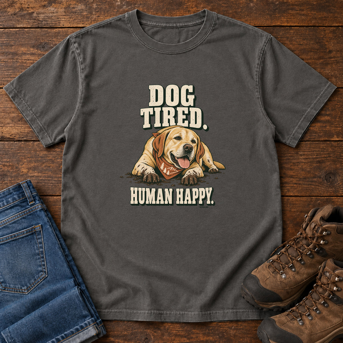 Dog Tired Human Happy T-Shirt in Pepper, front laid flat on wood, featuring a resting golden-brown dog wearing an orange bandana between cream slogan lettering.