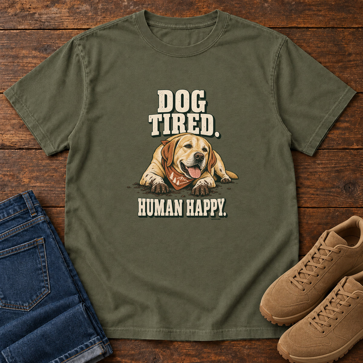 Dog Tired Human Happy T-Shirt in Sage, front laid flat on wood, featuring a resting golden-brown dog wearing an orange bandana between cream slogan lettering.